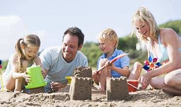 parents having fun on the beach with their kids building a sand castle