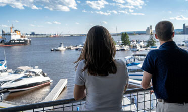 a couple lean over the railing of their balcony, overlooking the Duluth harbor