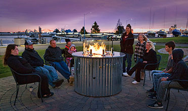 a group of 9 people with a baby in its mother's arms gathered around the fire table
