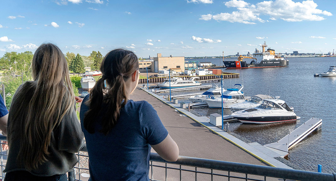 two guests stand on their balcony from the second floor of the resort, looking out over the harbor