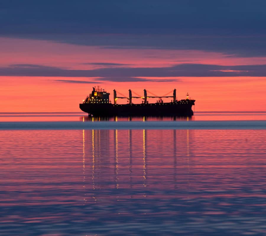 A sunset lights up the sky with pinks, oranges and blues while a ship is silhouetted against the colorful sky