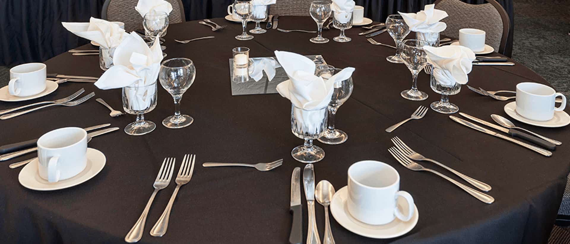 a round table is set with coffee cups, forks, knives and spoons